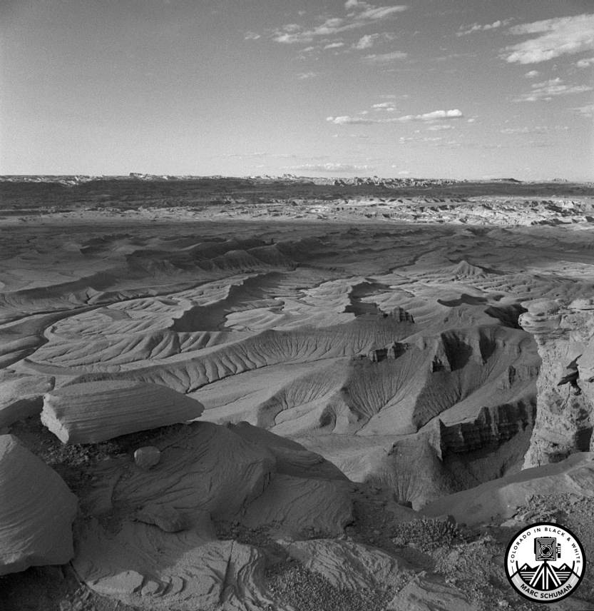 Black and white photograph of the eroded badlands below Moonscape Overlook in Utah at last light, with long shadows across the ridges